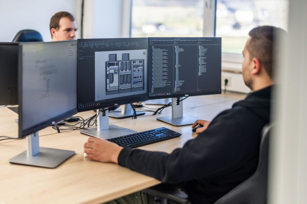 2 Personen sitzen am Schreibtisch und arbeiten am PC